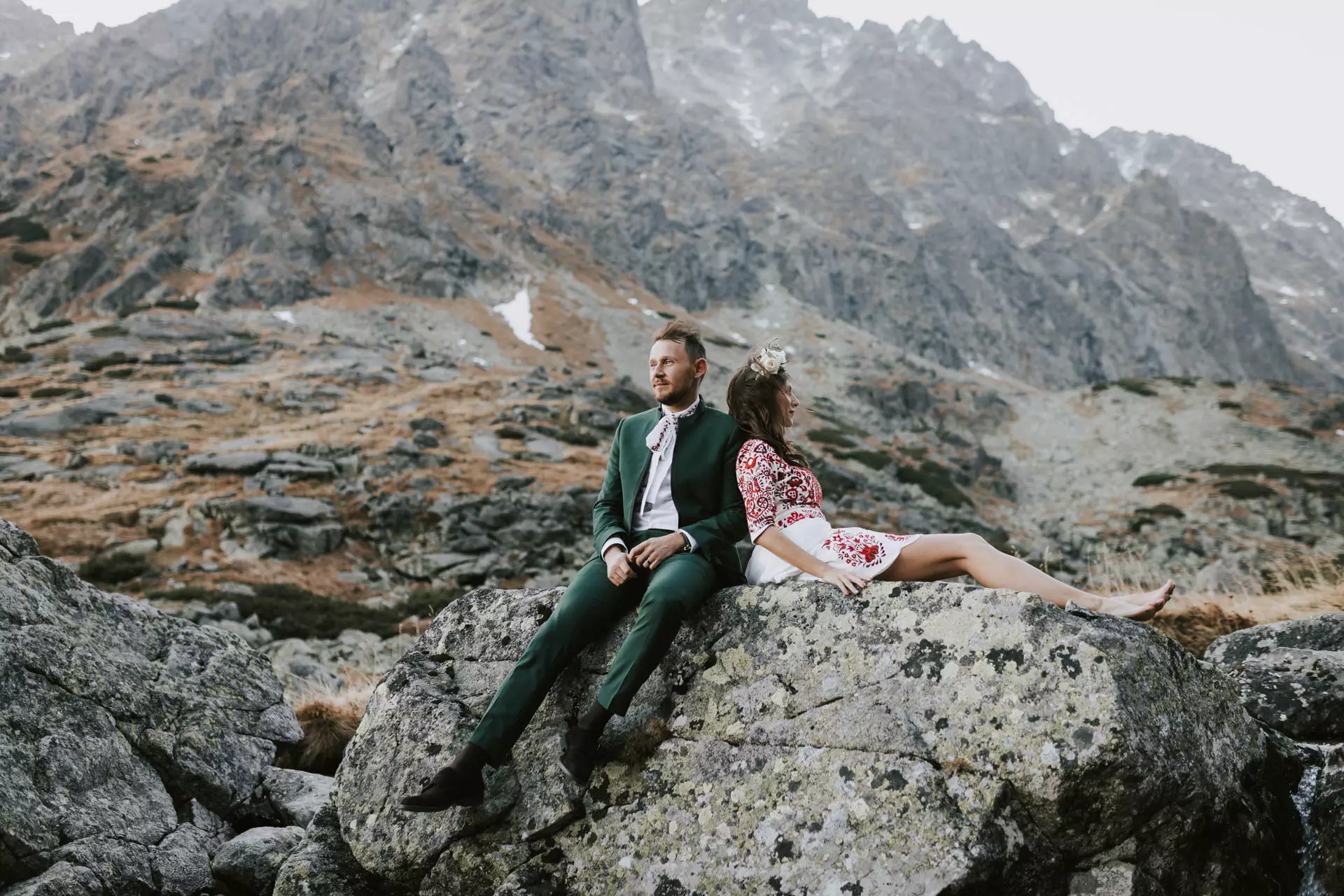 Svadobná fotka páru v horách sediacich na kameni